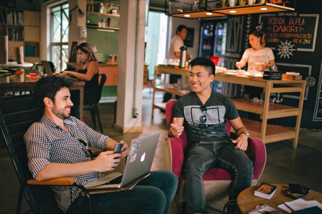 ¿Por qué entiendes inglés pero no puedes hablarlo? Two men enjoying a relaxed conversation with laptops in a cozy Brazilian café.